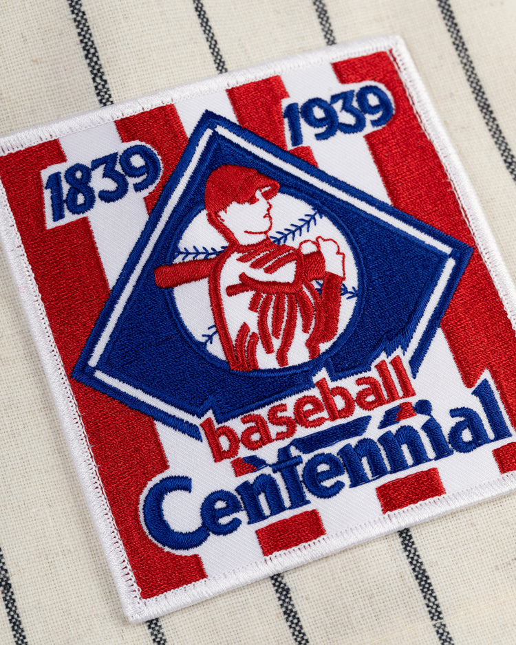 A red and white striped patch with a blue diamond, batter, and “1839 1939 Baseball Centennial” is stitched on the New York Knights 1939 Authentic Wool Home Baseball Jersey by Ebbets Field, inspired by The Natural and classic pinstriped style.