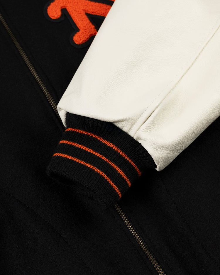 Close-up of the EFF New York Giants 1951 Authentic Wool & Leather Varsity Jacket sleeve in white leather with a black cuff and orange stripes, plus red-orange appliqué lettering—Polo Grounds-inspired style.