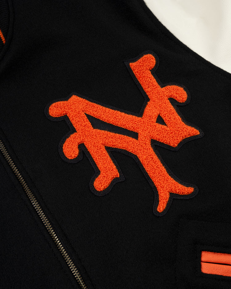 Close-up of the orange and black embroidered NY logo on dark fabric from the EFF New York Giants 1951 Authentic Wool & Leather Varsity Jacket, featuring a zipper and an orange-accented pocket inspired by the Polo Grounds.