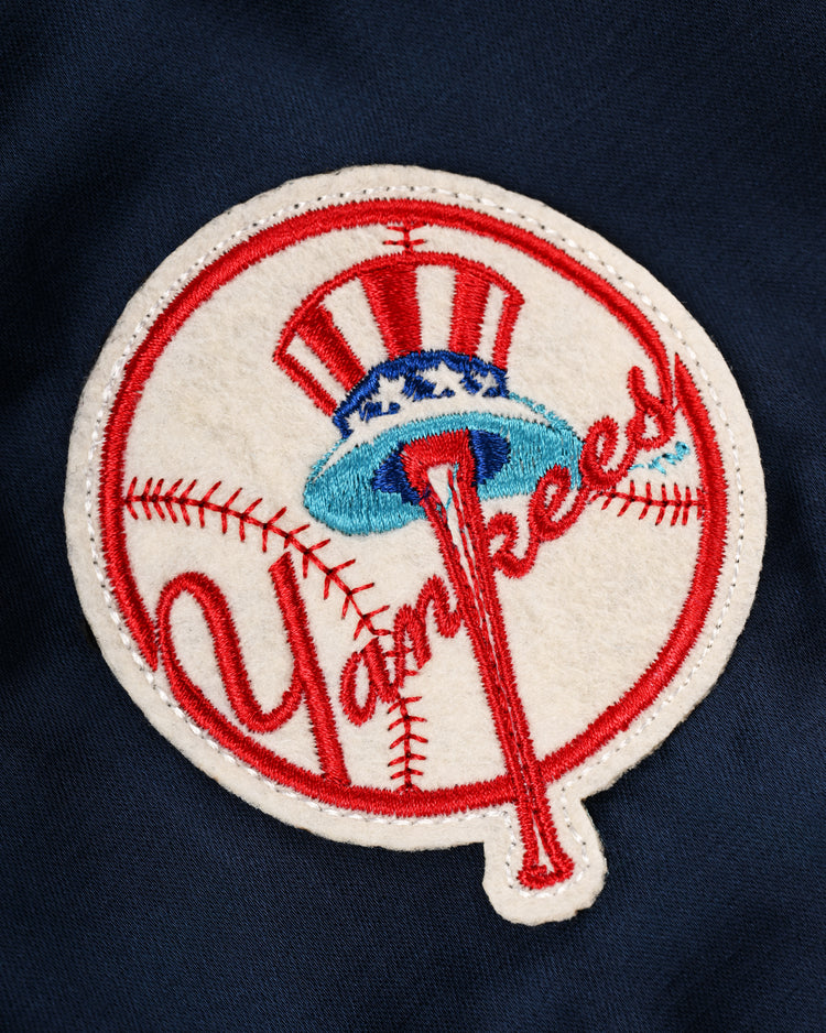 The EFF New York Yankees 1946 Satin Windbreaker Jacket features an embroidered NY Yankees logo with a baseball, bat-shaped “k”, and stars-and-stripes top hat—design inspired by the iconic 1946 jacket on dark blue satin.