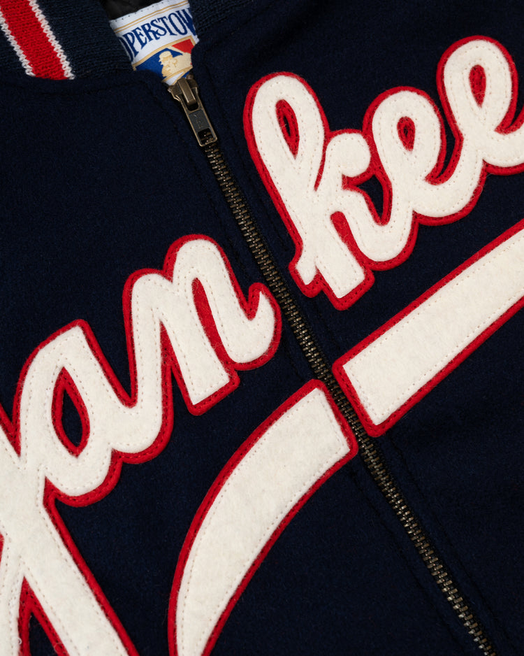 Close-up of the EFF New York Yankees 1947 Authentic All Wool Varsity Jacket featuring navy blue wool, a zipper, and white script lettering outlined in red—a tribute to the 1947 World Championship and Joe DiMaggio. Blue and white label at the collar.