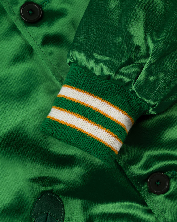 Close-up of the EFF Oakland Athletics 1968 Authentic All Satin Varsity Jacket sleeve, featuring green satin fabric, ribbed cuff with two white and a yellow stripe, black buttons, and detailed stitching.