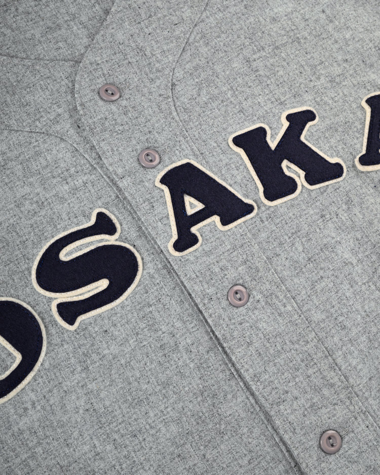 Close-up of the Ebbets Field Flannels Osaka Tigers 1959 Authentic Wool Road Baseball Jersey, in gray wool with navy letters outlined in cream spelling OSAKA, and gray buttons—recalling the classic Koshien Field style.