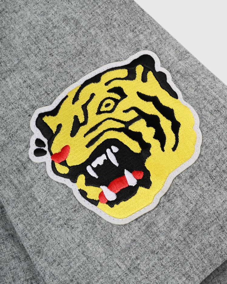 A close-up of a yellow tiger head patch, black stripes, red mouth, and white teeth sewn onto an Ebbets Field Flannels Osaka Tigers 1959 Authentic Wool Road Baseball Jersey.