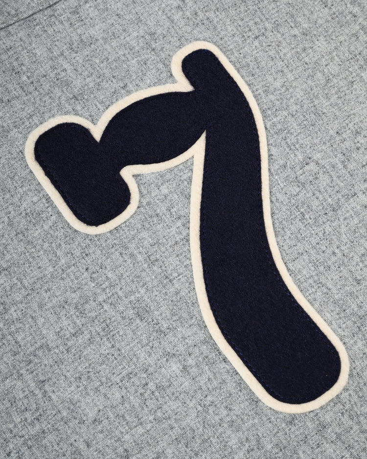 A dark blue, stylized number seven with a cream outline is sewn onto textured light gray wool, recalling the Osaka Tigers 1959 Authentic Wool Road Baseball Jersey by Ebbets Field Flannels.