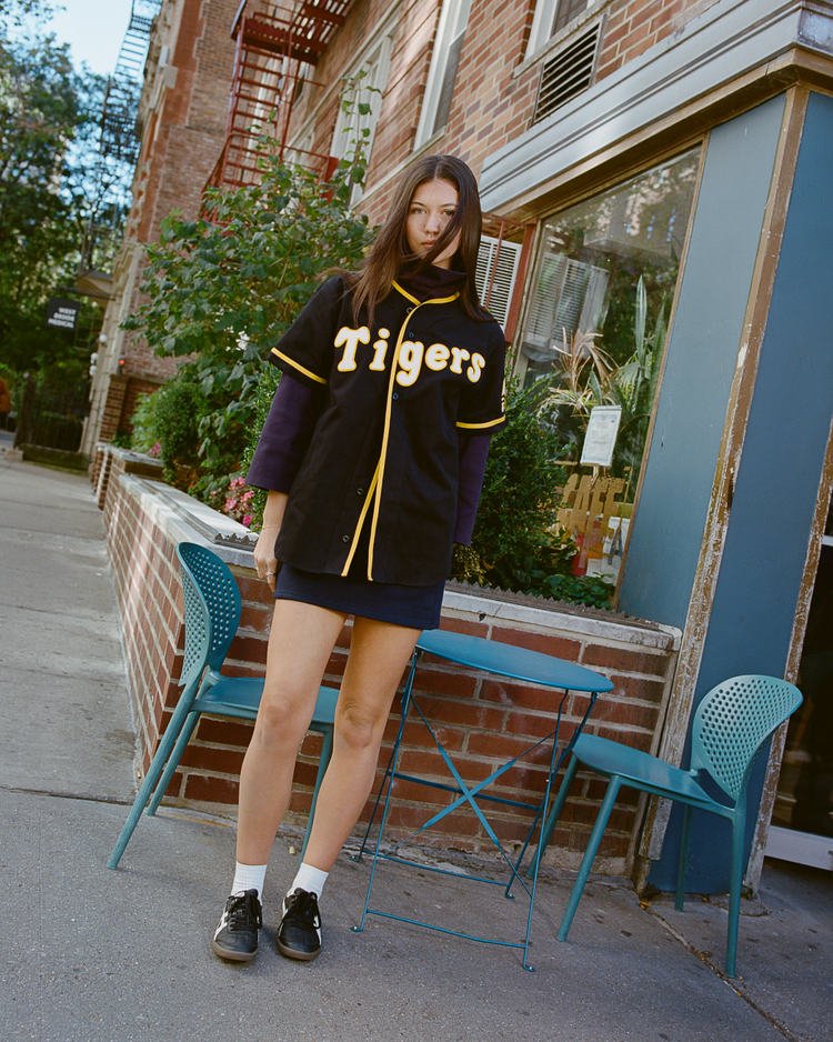 Person wearing a black Osaka Tigers jersey standing on a sidewalk with a building in the background