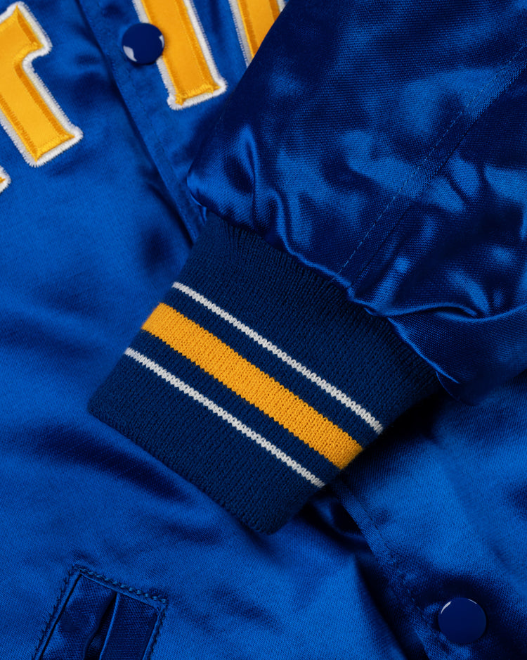 Close-up of a blue satin Seattle Mariners 1982 Authentic All Satin Varsity Jacket by EFF, showing the ribbed cuff with yellow and white stripes, part of the yellow lettering, blue snap buttons, and shiny fabric.