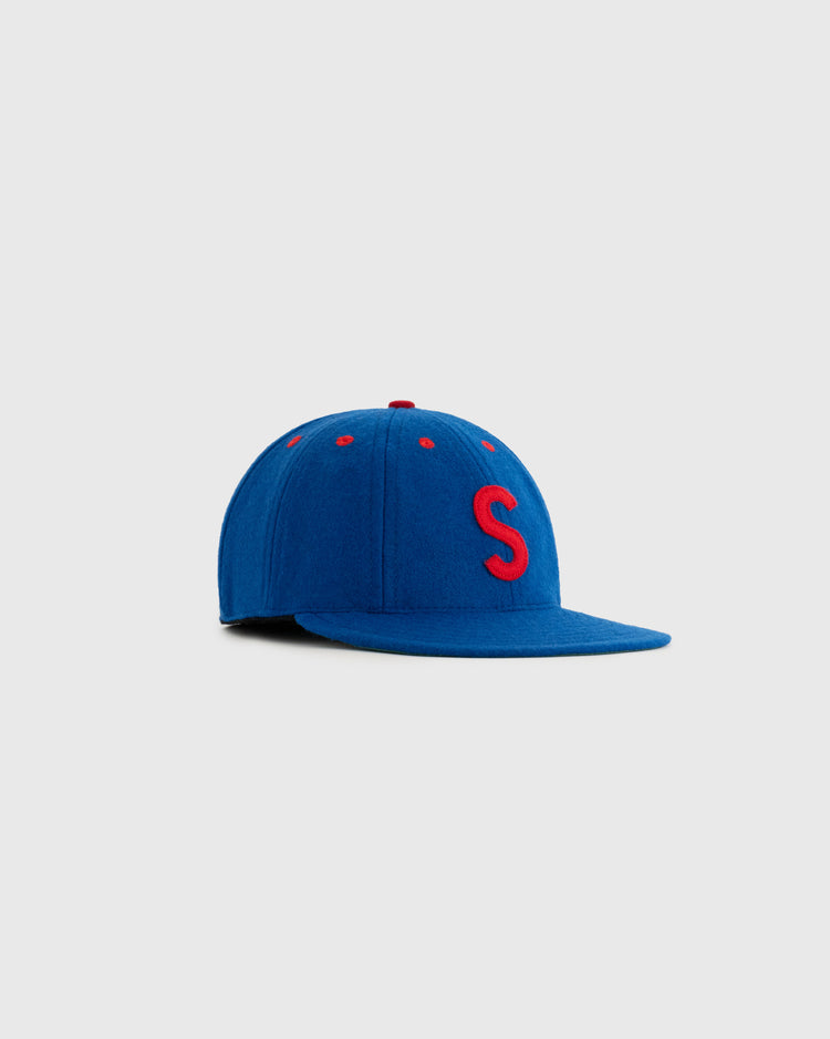The EFF Seattle Rainiers 1938 Authentic 8-Panel Wool Ballcap features blue wool, a red S on the front, and red accents on the button and eyelets, inspired by a classic Seattle Rainiers cap, shown on a light grey background.