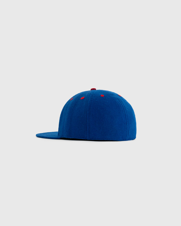 The EFF Seattle Rainiers 1938 Authentic 8-Panel Wool Ballcap, shown from the side on a light gray background, features blue wool, a flat brim, small red eyelets, and a red top button.