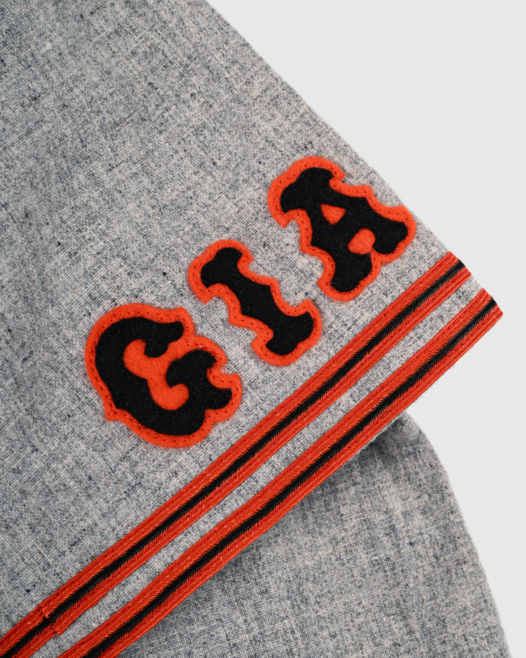 A close-up of grey wool from the Ebbets Field Flannels Tokyo Kyojin 1961 Authentic Road Baseball Jersey, showing bold black and orange terry letters “GIA” and two parallel stripes inspired by the classic Tokyo Giants design.