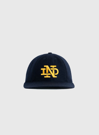 The EFF University of Notre Dame 1943 Authentic Wool 8-Panel Ballcap showcases a navy design with a yellow interlocking ND logo, honoring the schools football championship, set against a plain light gray background.