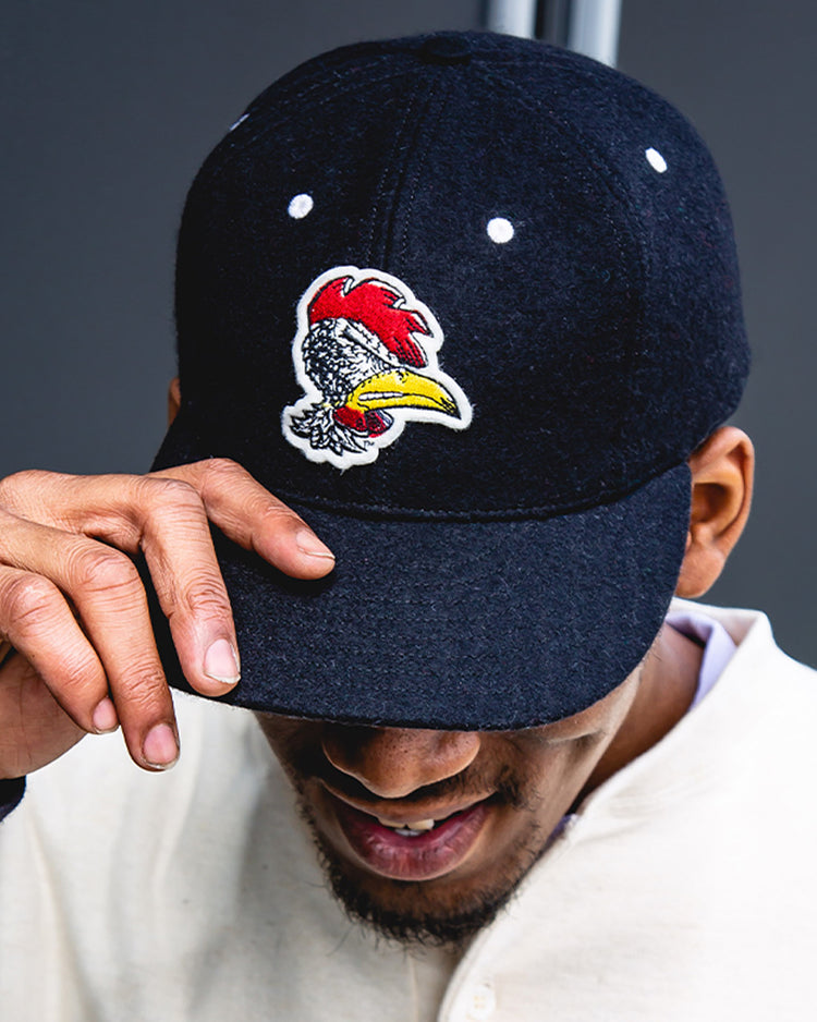 A person wearing the EFF University of South Carolina Gamecocks Mascot Vintage Ballcap, featuring a colorful rooster patch, tilts the black cap’s brim and smiles slightly in a light-colored shirt.