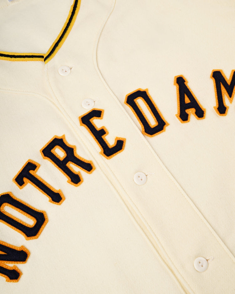 Close-up of the Ebbets Field University of Notre Dame 1956 Authentic Wool Home Baseball Jersey, featuring cream wool, NOTRE DAM in navy and gold across the chest, and yellow/navy collar trim for classic Notre Dame style.
