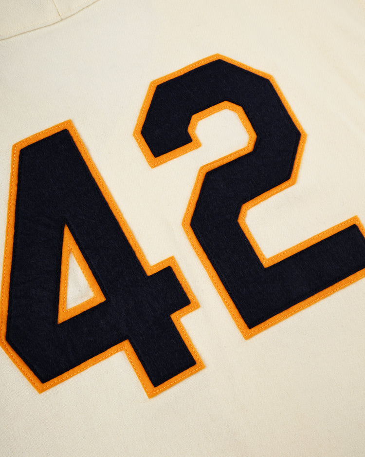 Close-up of the University of Notre Dame 1956 Authentic Wool Home Baseball Jersey by Ebbets Field in cream, showcasing a bold dark blue number 42 with an orange outline—a tribute to classic Fighting Irish style.