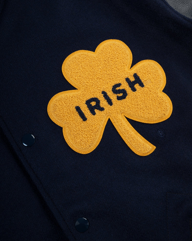 A yellow shamrock patch with IRISH in black is sewn onto the dark navy University of Notre Dame Authentic Wool & Leather Varsity Jacket by EFF, evoking the style of a classic letterman or vintage Notre Dame football jacket.