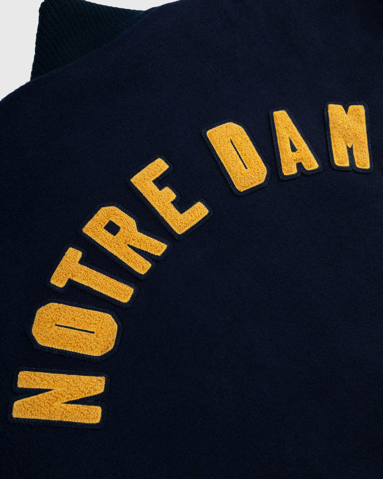Close-up of a navy blue EFF University of Notre Dame Authentic Wool & Leather Varsity Jacket featuring large yellow NOTRE DAM letters in an arch.