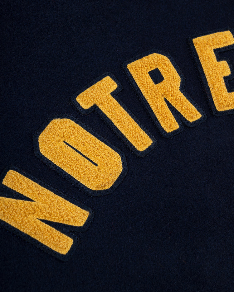 Close-up of yellow textured NOTRE letters on dark blue fabric from the EFF University of Notre Dame Authentic Wool & Leather Varsity Jacket.