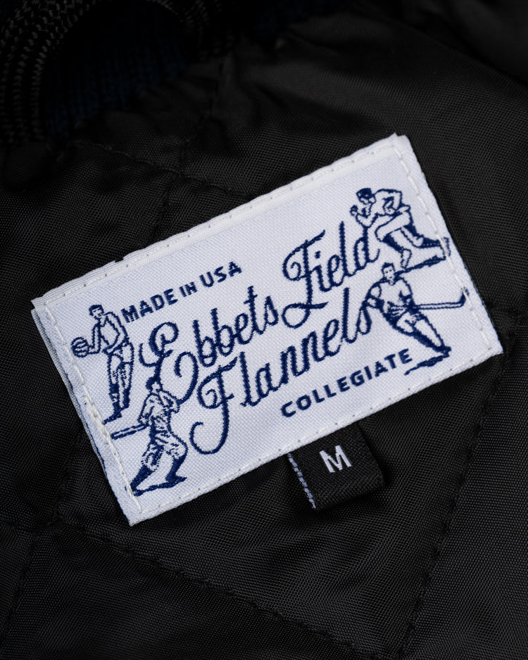 A white EFF label reads Collegiate, Made in USA with blue vintage baseball art—ideal for the University of Notre Dame Authentic Wool & Leather Varsity Jacket. A small black tag below marks size M.