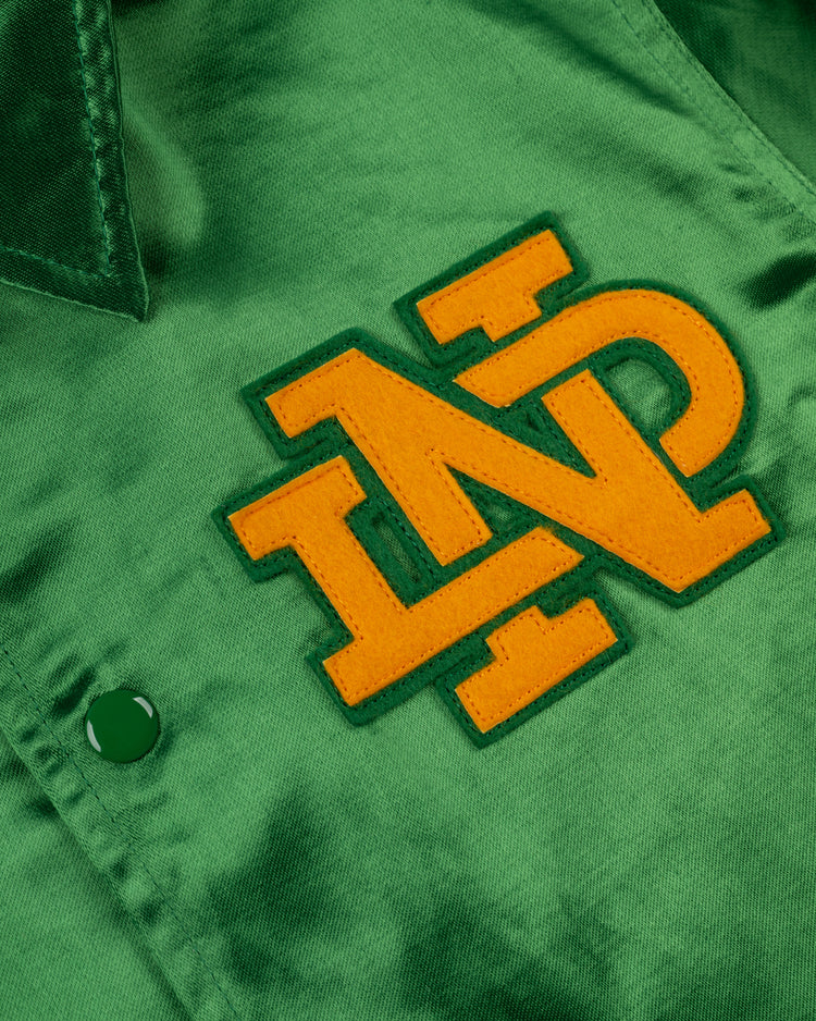Close-up of green fabric from the EFF University of Notre Dame Satin Windbreaker Jacket, featuring a yellow and green NP embroidered patch and a green button.