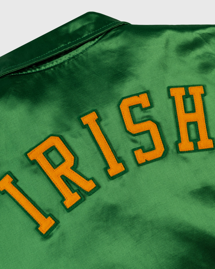 The EFF University of Notre Dame Satin Windbreaker Jacket features a green vintage-inspired design with large yellow block letters spelling IRISH stitched on the back, prominently shown in the images upper portion.