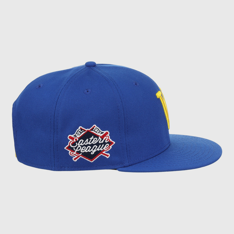 The Vermont Mariners EFF MiLB Vintage Snapback by Ebbets Field Flannels is a blue cap with a flat brim, yellow front logo, and an Eastern League patch with crossed bats. It features a snapback adjustable fit and is part of the Vintage Minor League collection.