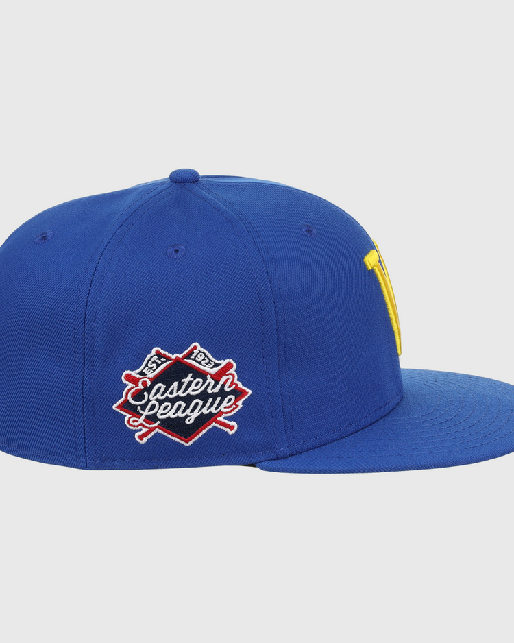 The Vermont Mariners EFF MiLB Vintage Snapback by Ebbets Field Flannels is a blue cap with a flat brim, yellow front logo, and an Eastern League patch with crossed bats. It features a snapback adjustable fit and is part of the Vintage Minor League collection.