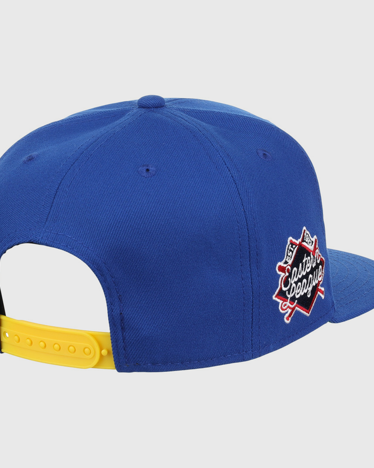 The Vermont Mariners EFF MiLB Vintage Snapback by Ebbets Field Flannels is a blue cap with a yellow adjustable strap and Classic League patch with crossed bats, inspired by the Vermont Mariners. Shown from back and side.