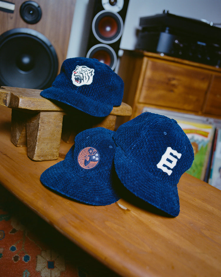 Group picture of the Tokyo Giants, Osaka Tigers, and Hiroshima Carp
ball caps on a wooden table. Made with genuine indigo-dyed corduroy fabric and featuring the team logos on the front of the caps.