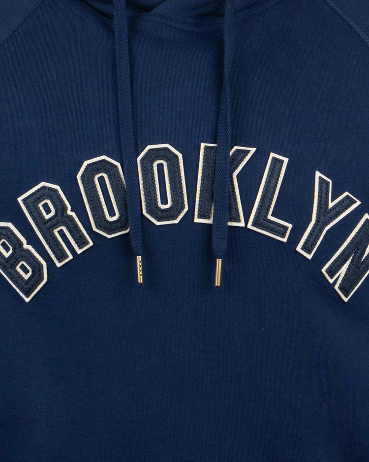 The EFF Brooklyn Eagles French Terry Script Hooded Sweatshirt is navy blue with BROOKLYN in bold white letters on the chest and features metal-tipped drawstrings, paying tribute to the Brooklyn Eagles.