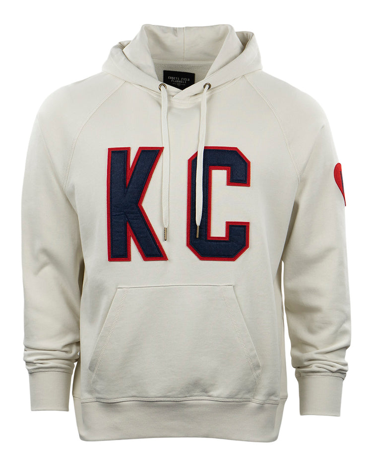 The EFF Kansas City Monarchs French Terry Script Hooded Sweatshirt is cream-colored, with a front pocket, large navy and red KC letters on the chest, and a small red heart on the upper left sleeve.