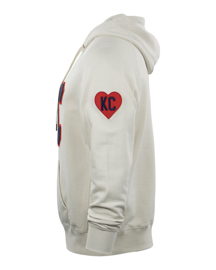Side view of the EFF Kansas City Monarchs French Terry Script Hooded Sweatshirt in cream, featuring a red heart KC patch on the upper sleeve, front pocket, and drawstrings. Inspired by the historic baseball team.