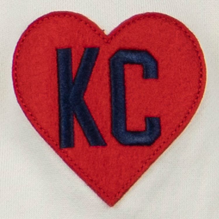 The EFF Kansas City Monarchs French Terry Script Hooded Sweatshirt features a white base and a red heart-shaped patch with dark blue KC letters, inspired by the historic Negro Leagues team.
