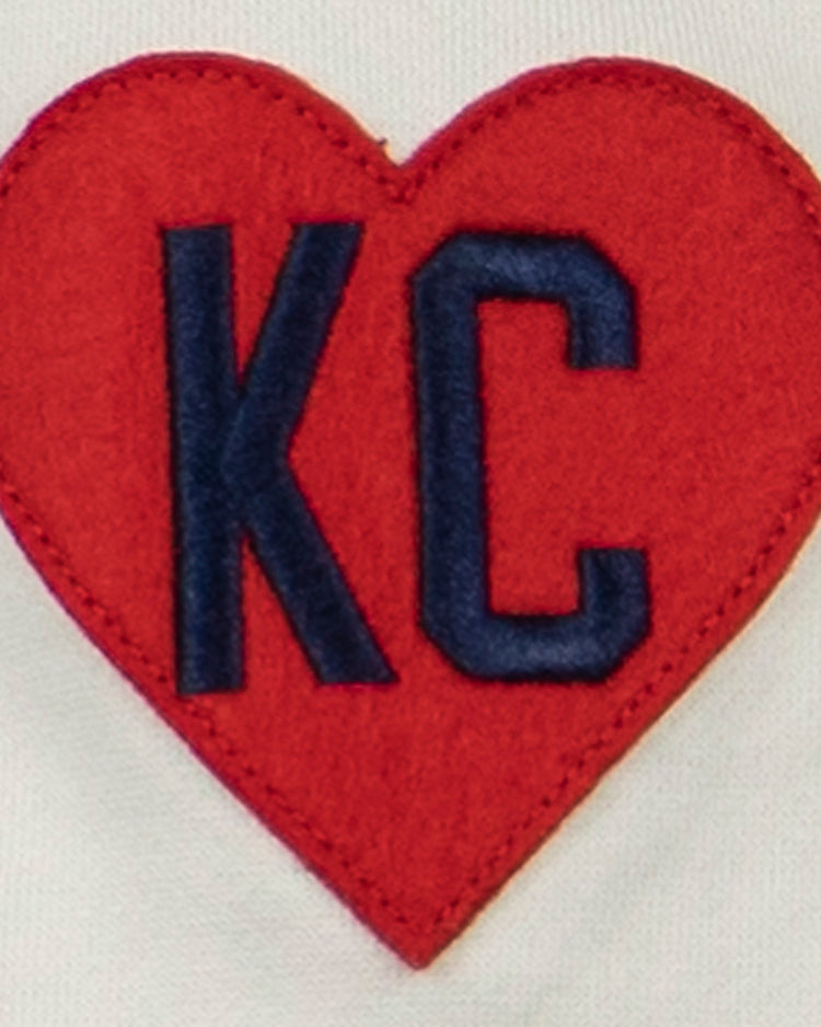 The EFF Kansas City Monarchs French Terry Script Hooded Sweatshirt features a white base and a red heart-shaped patch with dark blue KC letters, inspired by the historic Negro Leagues team.