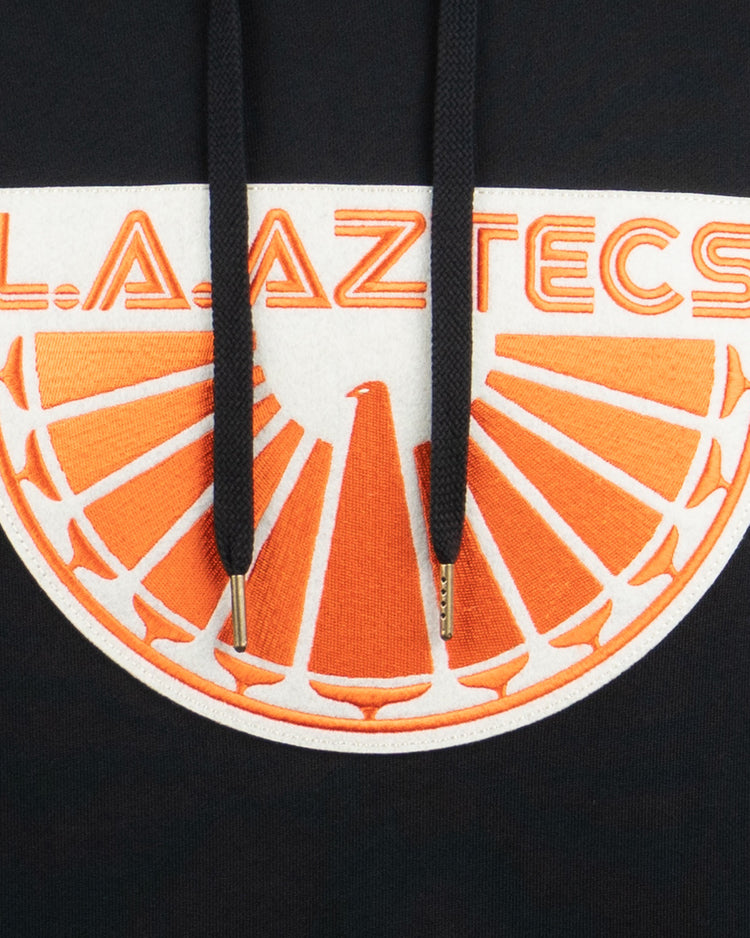 Celebrate the iconic NASL team with the EFF Los Angeles Aztecs French Terry Script Hooded Sweatshirt, featuring L.A. AZTECS in orange above a bold orange and white half-sun and bird design on black.