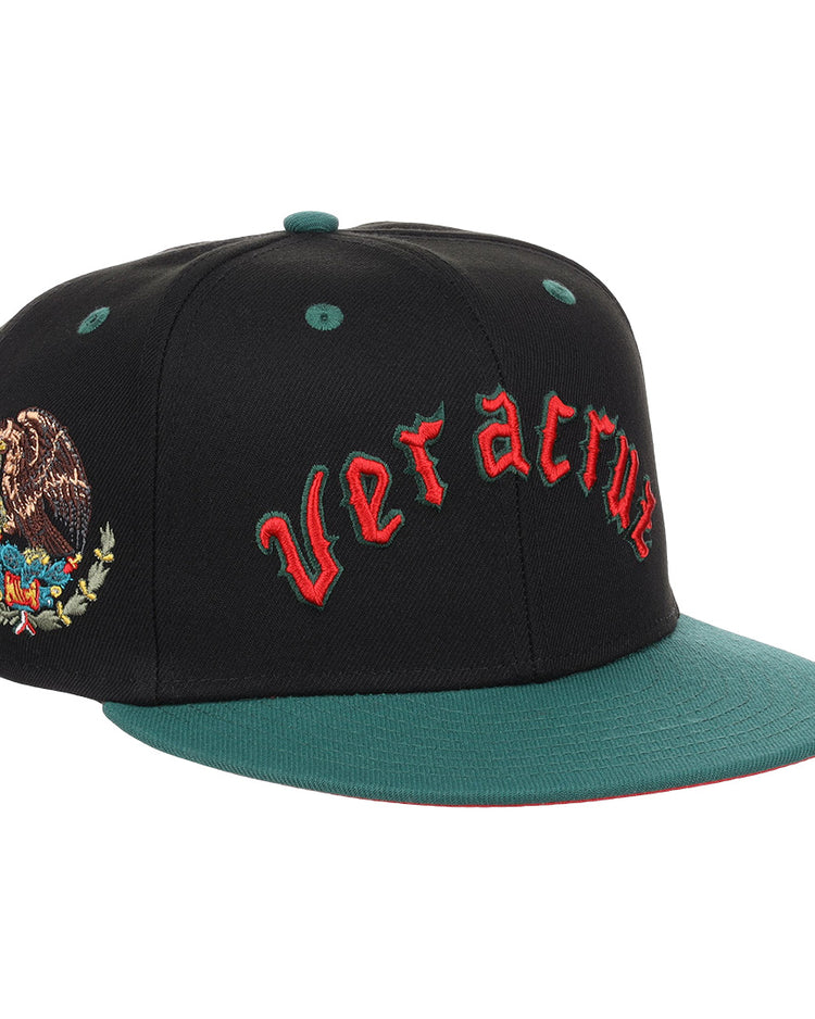 The EFF Veracruz Azules NLB Flip Fitted Ballcap is a black and green cap with “Veracruz” in red front embroidery, the Mexican emblem on the side, honoring the legacy of the Mexican League.