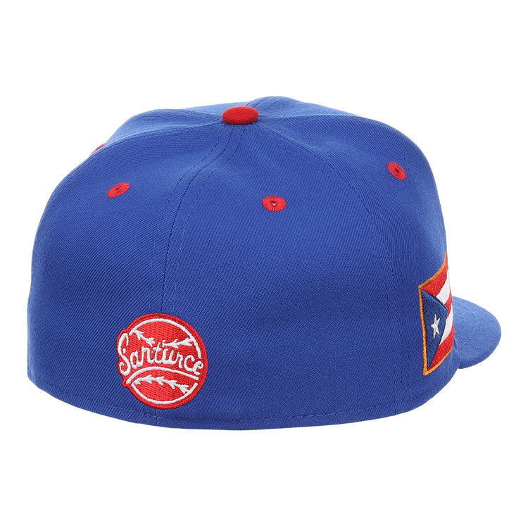 The EFF Santurce Cangrejeros NLB Flip Fitted Ballcap is a blue cap with red accents, a circular Santurce patch on the back, a Puerto Rican flag patch on the side, and is inspired by Puerto Rican League legends like Roberto Clemente.