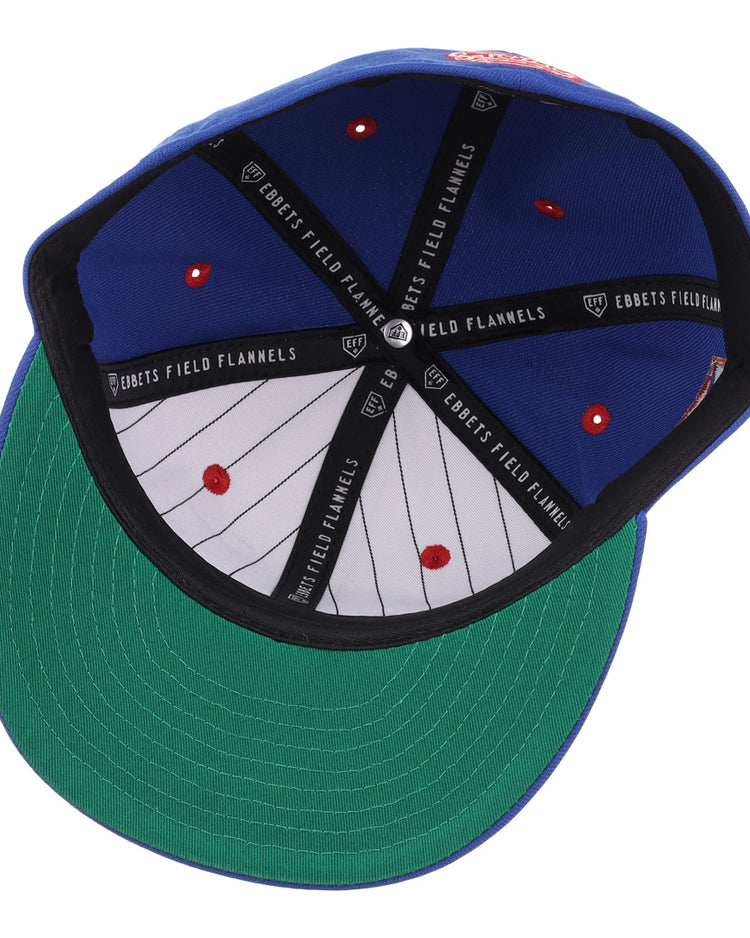 The image shows the inside of the Santurce Cangrejeros NLB Flip Fitted Ballcap by EFF, featuring a blue crown, green underbill, red stitch dots, black EFF-labeled taping, and thin black stripes—details inspired by classic Puerto Rican League styles.