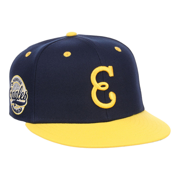The EFF Newark Eagles NLB Flip Fitted Ballcap is navy blue and yellow with a yellow brim, features a large embroidered yellow C on the front, and has an American Eagles circular patch on the side.