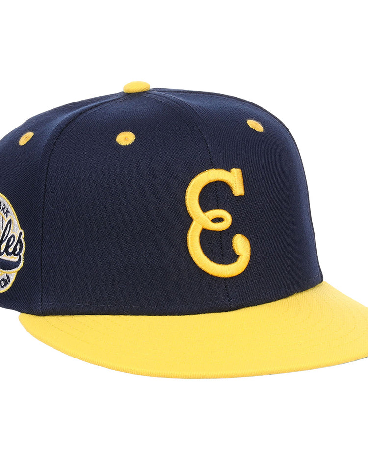 The EFF Newark Eagles NLB Flip Fitted Ballcap is navy blue and yellow with a yellow brim, features a large embroidered yellow C on the front, and has an American Eagles circular patch on the side.