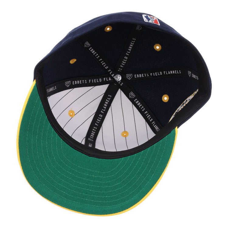 The image shows the inside of an EFF Newark Eagles NLB Flip Fitted Ballcap, featuring a green underbrim, yellow visor edge, striped white lining, embroidered logo, and a sweatband with repeated EBBETS FIELD FLANNELS text.