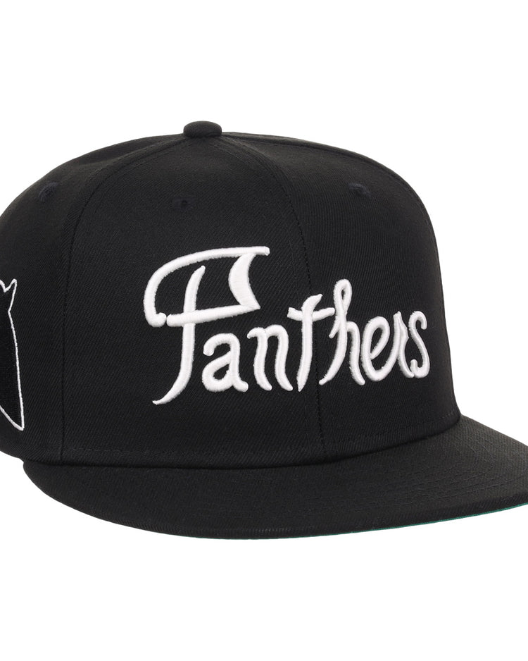 The EFF Montreal Black Panthers NLB Flip Fitted Ballcap is a vintage-inspired black cap with Panthers in bold white script on the front and a small embroidered black panther head with red eyes and mouth on the side.