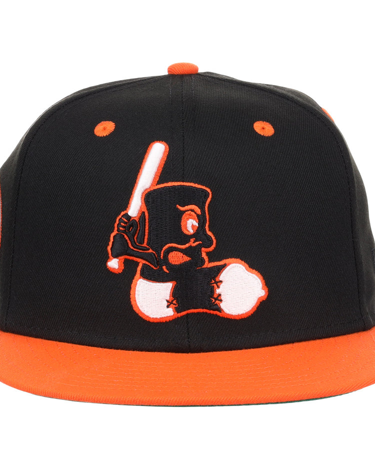 The EFF Baltimore Black Sox NLB Flip Fitted Ballcap features black and orange colors, a cartoon character with a bat embroidered on the front, and vintage-inspired orange brim and button for a standout look.