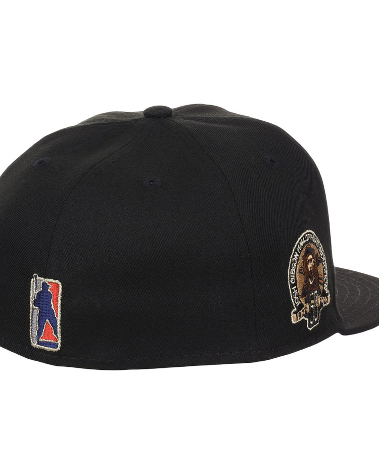 The EFF Homestead Grays Josh Gibson Fitted Ballcap in black is shown from an angled rear view, featuring a multicolor embroidered back logo and a lion patch with text on the left side, inspired by classic Negro Leagues cap designs.