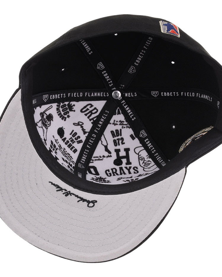 The Homestead Grays Josh Gibson Fitted Ballcap - Black by EFF is shown from above, highlighting its inner lining with EFF branding and black graphic designs and text on the white underside of the brim.