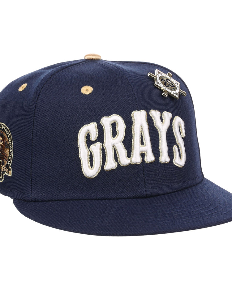 The EFF Homestead Grays Josh Gibson Fitted Ballcap in navy features “GRAYS” in large white letters, a team patch on the side, and a vintage baseball pin above the logo.