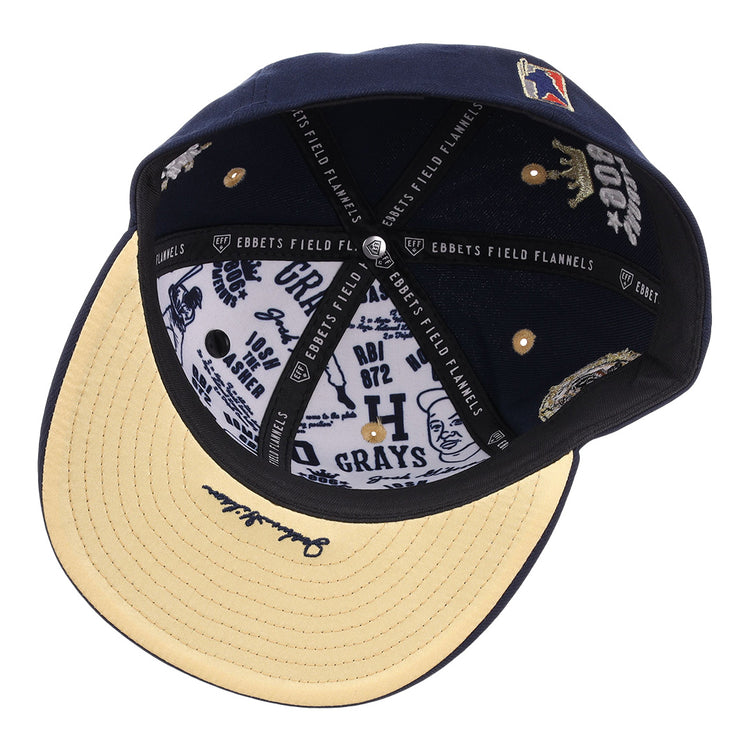 The Homestead Grays Josh Gibson Fitted Ballcap by EFF is shown from underneath, displaying its beige brim, black EFF-labeled inner bands, and a white lining decorated with various blue printed logos and text.