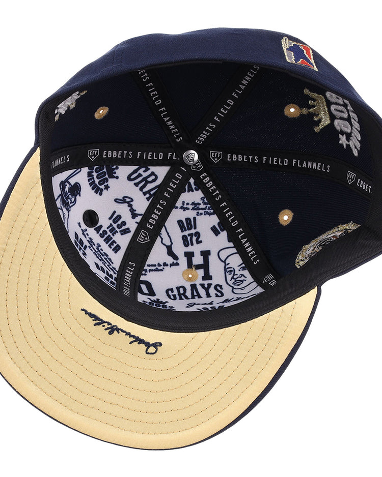 The Homestead Grays Josh Gibson Fitted Ballcap by EFF is shown from underneath, displaying its beige brim, black EFF-labeled inner bands, and a white lining decorated with various blue printed logos and text.