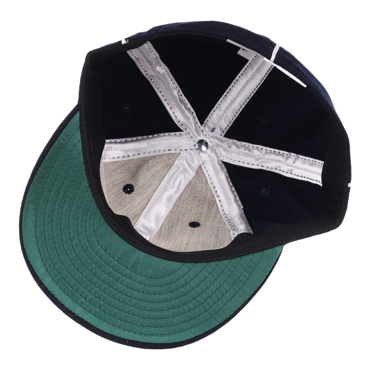 The image displays the inside of the EFF Santa Cruz Crabs 1908 Vintage Ballcap, with a green bill underside, black crown interior, white stitched seams, and a genuine grey wool baseball cloth panel.