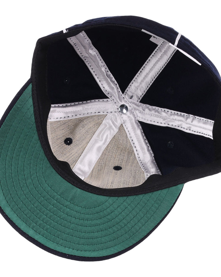 The image displays the inside of the EFF Santa Cruz Crabs 1908 Vintage Ballcap, with a green bill underside, black crown interior, white stitched seams, and a genuine grey wool baseball cloth panel.