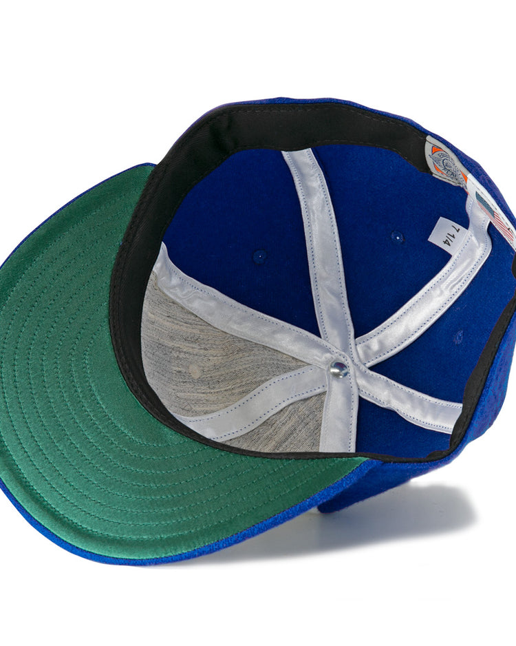The Hank Aaron 1973 Signature Series Ballcap by Ebbets Field Flannels is a blue vintage wool cap shown from below, highlighting its green under-brim, white hatband, and inner structure with a central metal button.